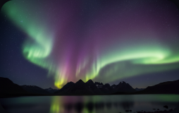 Aurora borealis glowing green over a lake and mountains near Reykjavík